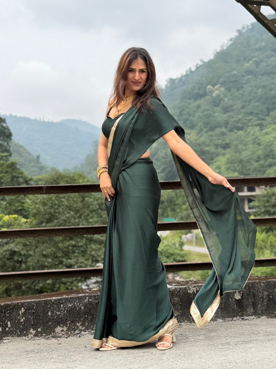 Woman on a bridge in the Pine Hush After Dark Saree, pallu lifted and flowing — deep bottle green with gold lace border