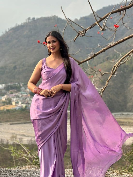 Woman in a purple saree standing outdoors with mountains and trees in the background