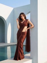 Woman in Cocoa Mirage brown chiffon saree leaning against a white arch, hand in hair, poolside