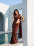 Woman in Cocoa Mirage brown chiffon saree leaning against a white arch, hand in hair, poolside