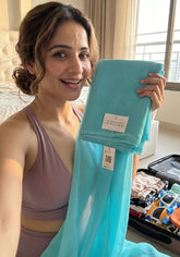 A woman in a purple sports bra holds up a folded light blue sheer fabric item with a visible brand tag reading &