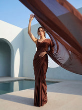 Woman in Cocoa Mirage brown chiffon saree with pallu billowing dramatically beside a white archway pool