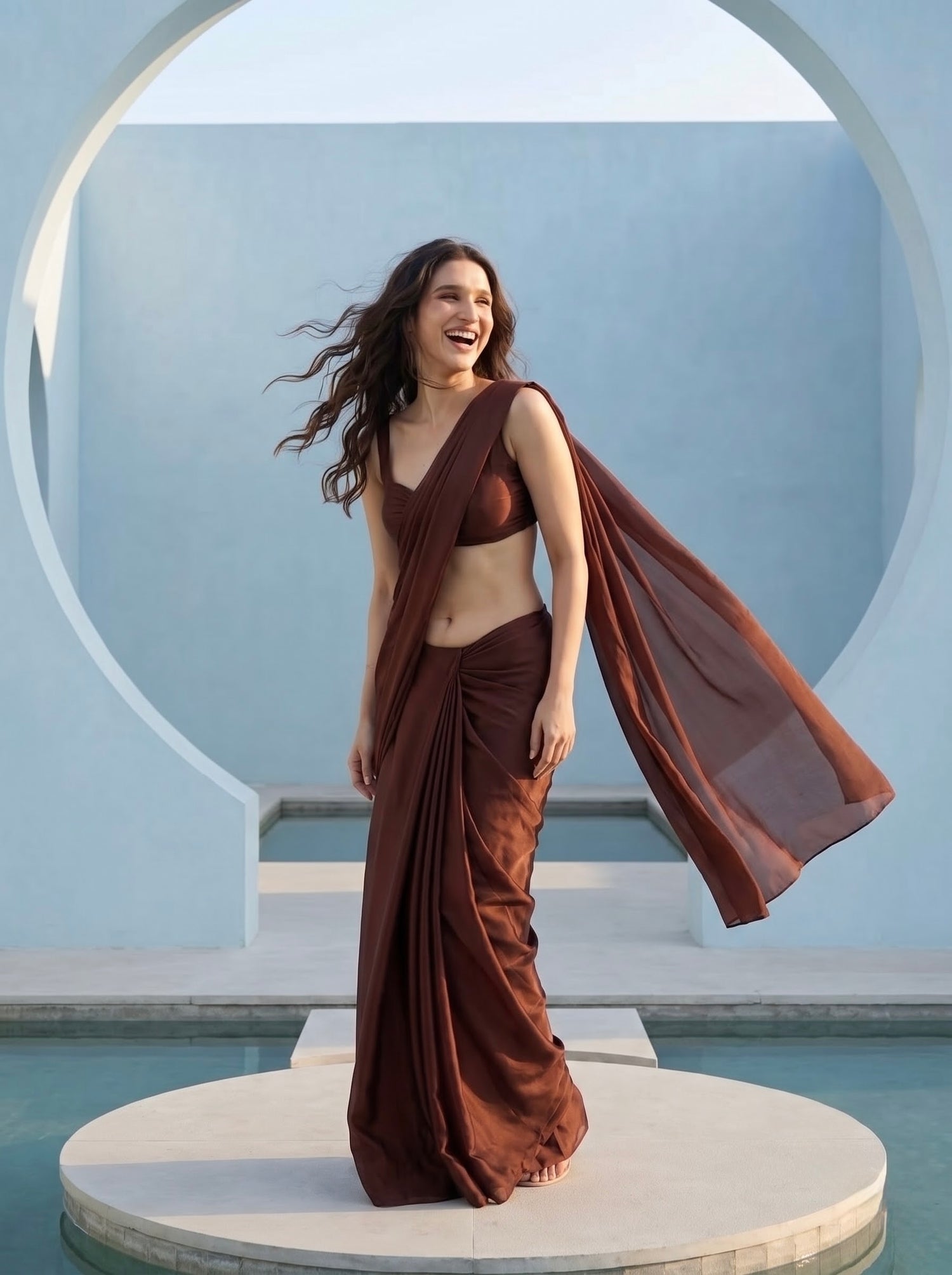Woman laughing in Cocoa Mirage brown chiffon saree under a domed white archway, hair in motion