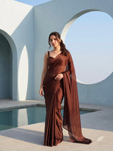 Full-length shot of woman in Cocoa Mirage brown chiffon saree standing beside a pool, white circular archway behind her